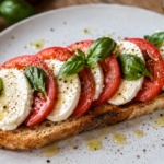 Geröstetes Sauerteigbrot mit frischen Tomaten-Mozzarella und Basilikum, verfeinert mit Olivenöl und schwarzem Pfeffer.